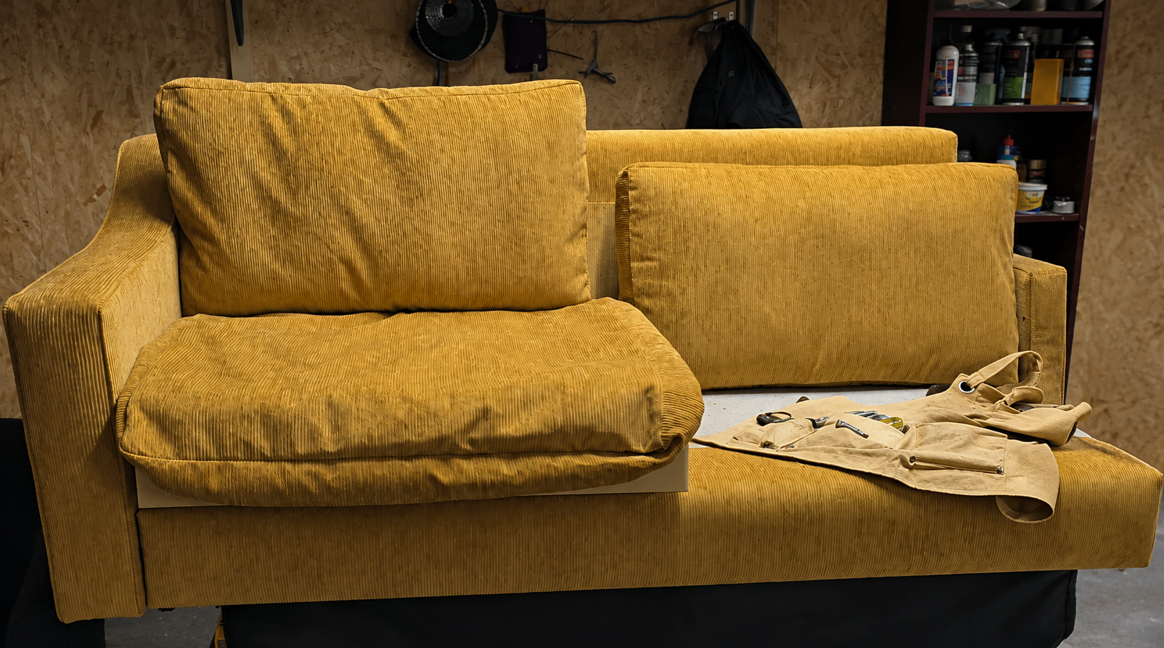 A mustard corduroy sofa part-way through renewal in the Edinburgh workshop, cushions removed and tool roll laid out