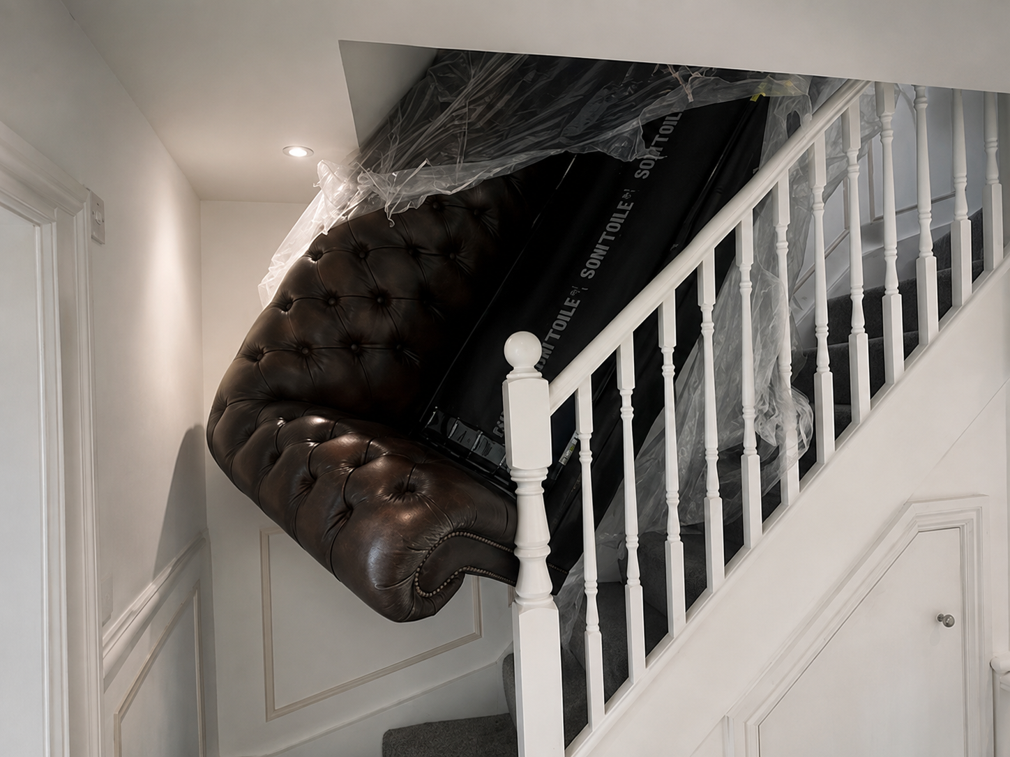 Large dark leather Chesterfield sofa wedged on a narrow staircase