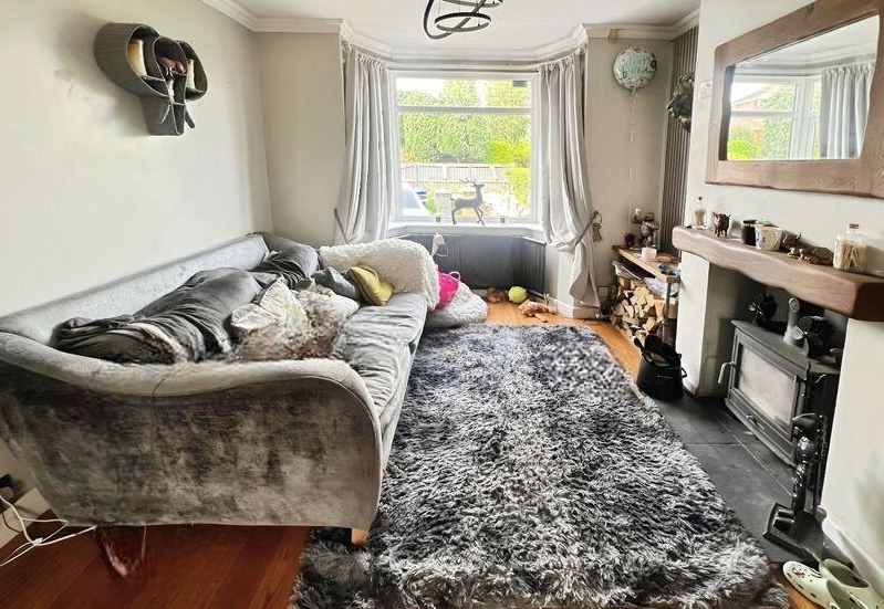 A grey sofa that is too large for the proportions of a narrow UK living room with a bay window and fireplace