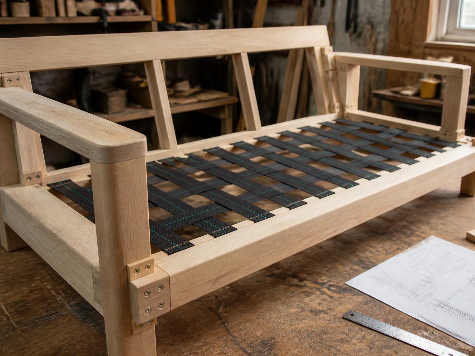Bare kiln-dried hardwood sofa frame with glued and screwed corner blocks and tensioned webbing on a workshop bench